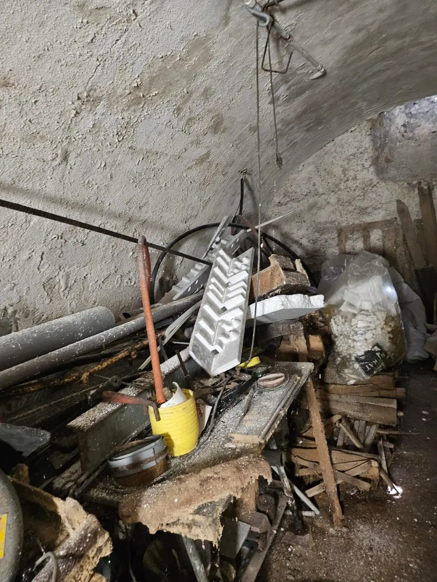 Cave voûtée encombrée de gravats et de bois avant curage