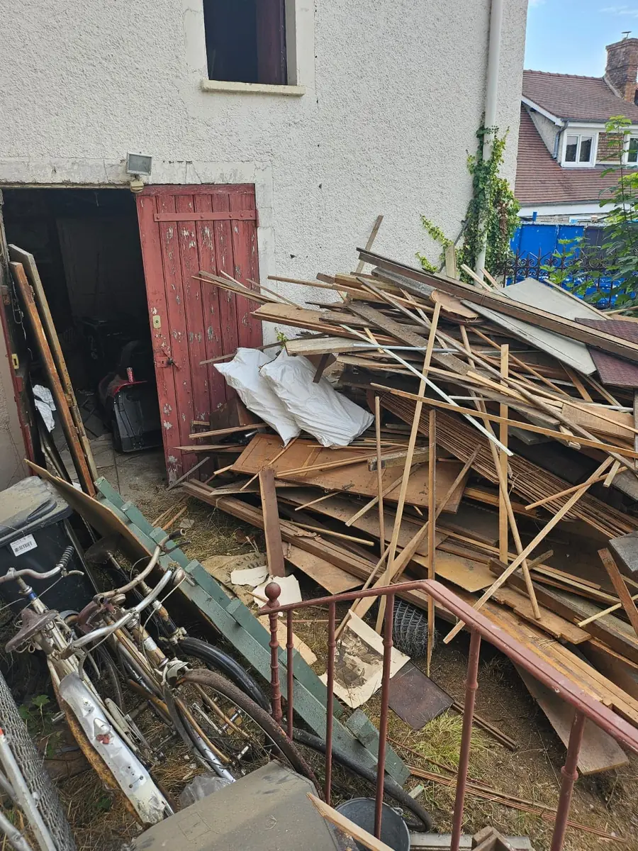 Bois de charpente et gravats rassemblés devant une maison en travaux
