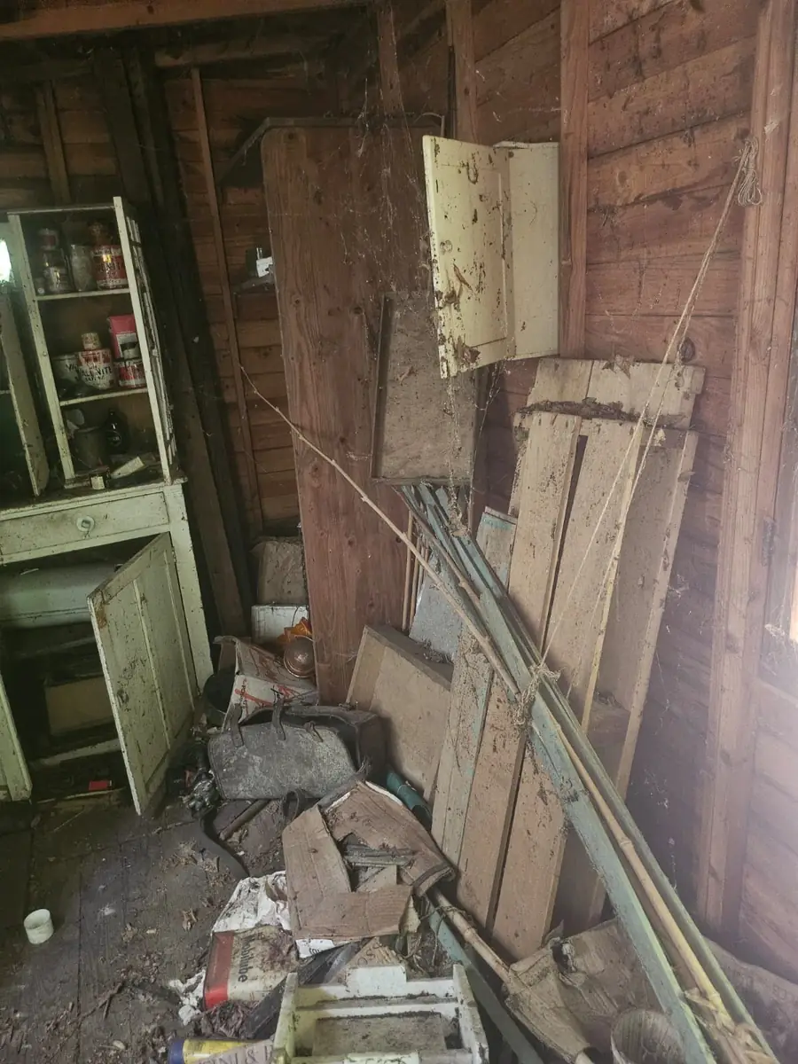 Remise encombrée de planches, de meubles et de gravats avant intervention